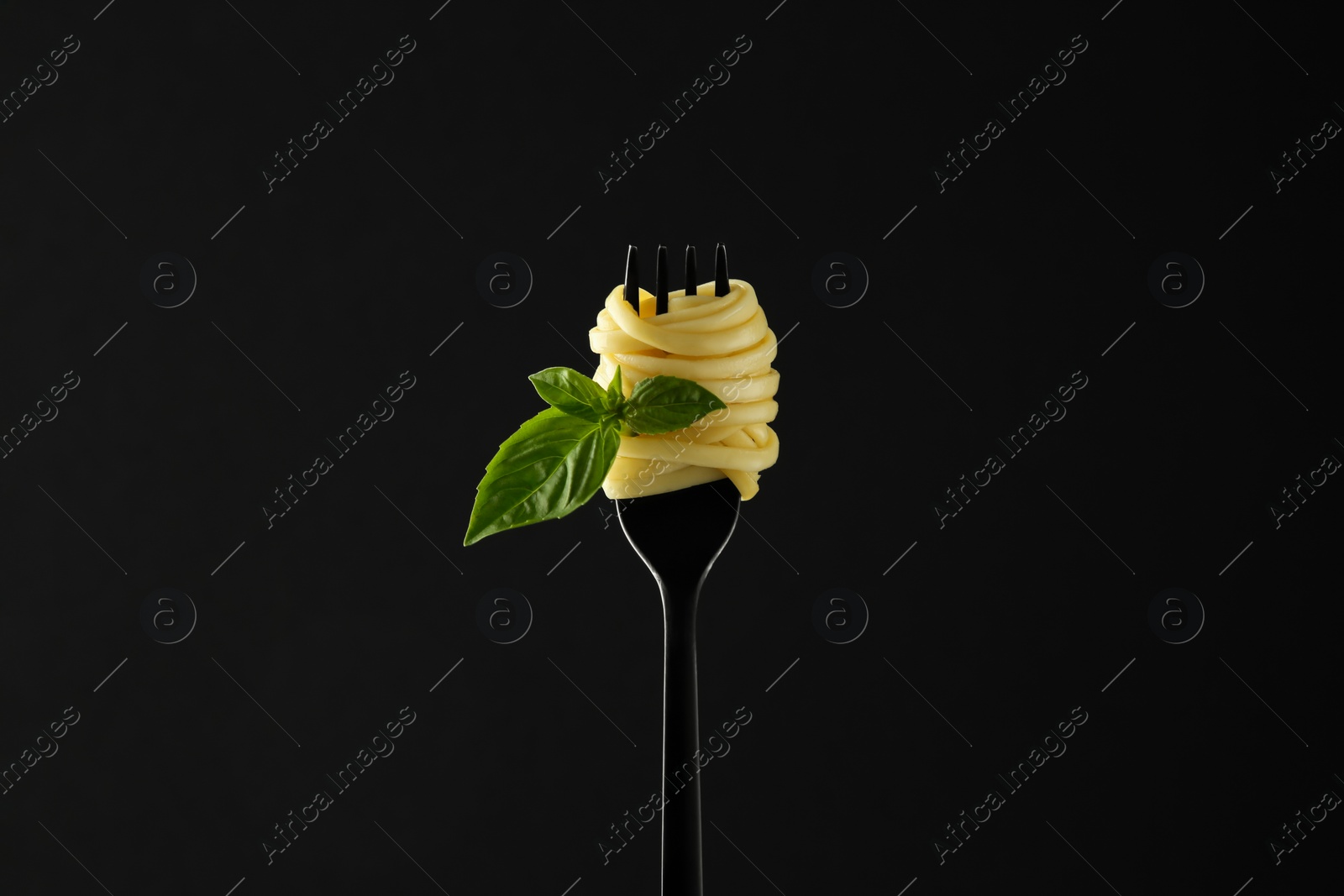 Photo of Fork with tasty pasta and basil on black background
