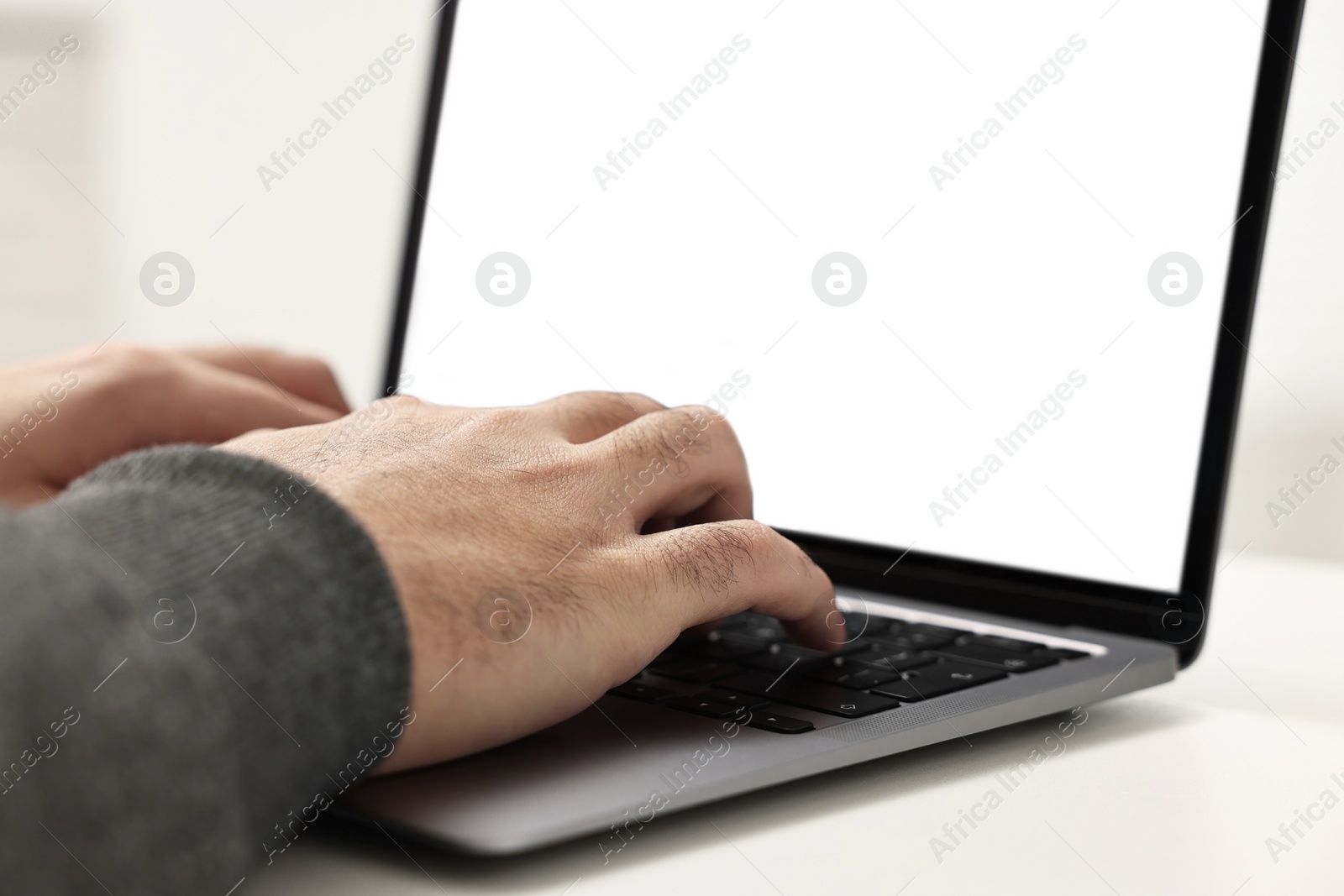 Photo of E-learning. Young man using laptop at white table, closeup