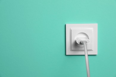 Photo of Power socket with inserted plug on turquoise wall, space for text. Electrical supply