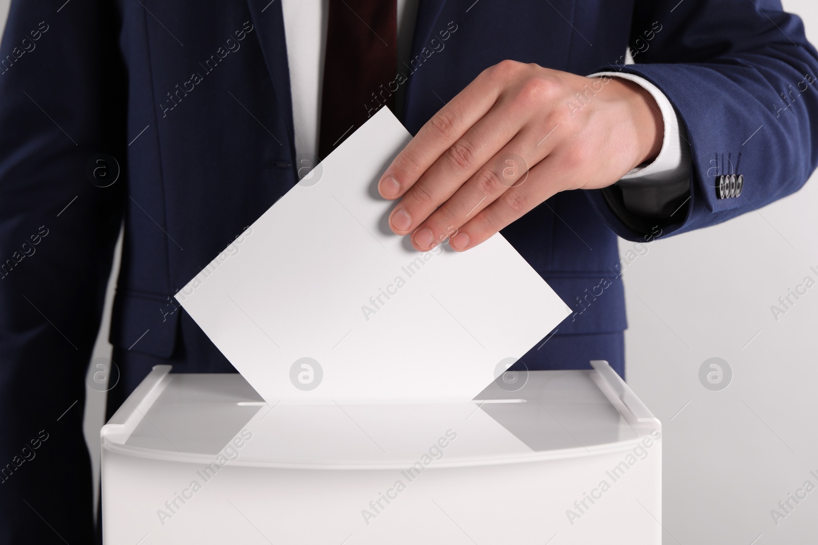 Photo of Man putting his vote into ballot box on light grey background, closeup