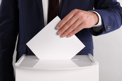 Man putting his vote into ballot box on light grey background, closeup