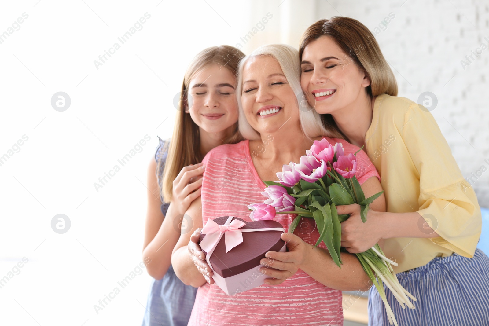 Photo of Young woman with daughter congratulating mature family member at home. Happy Mother's Day