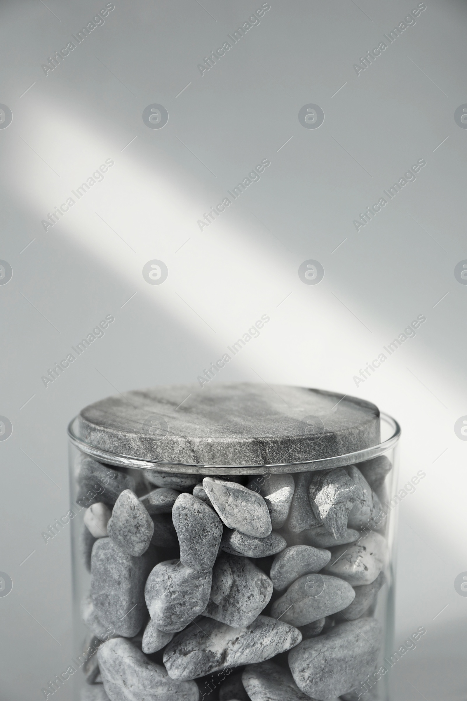 Photo of Presentation for product. Glass container with stones on light grey background. Space for text