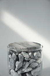 Photo of Presentation for product. Glass container with stones on light grey background. Space for text