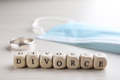 Photo of Cubes with word Divorce, protective mask and wedding ring on white wooden table, closeup