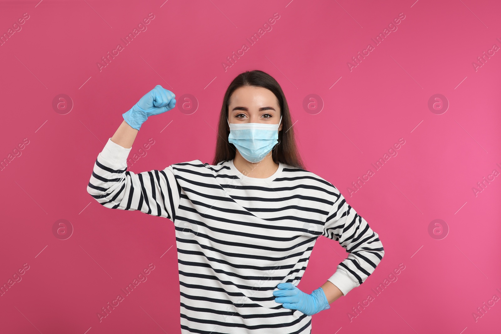 Photo of Woman with protective mask and gloves showing muscles on pink background. Strong immunity concept