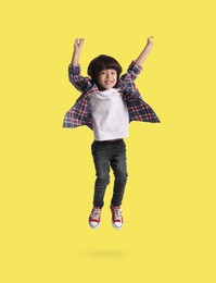 Happy boy jumping on yellow background, full length portrait