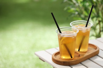 Photo of Plastic cups of tasty iced tea with lemon on white wooden table against blurred background, space for text