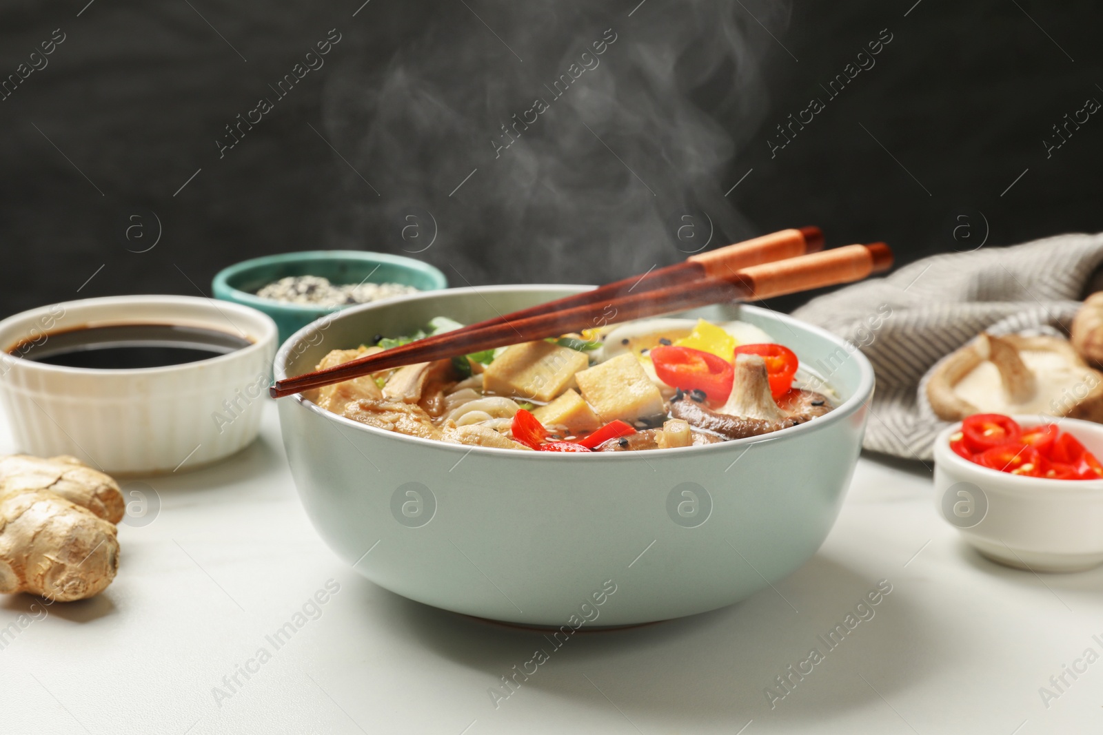 Image of Bowl of hot ramen, ingredients and chopsticks on white table, closeup. Noodle soup