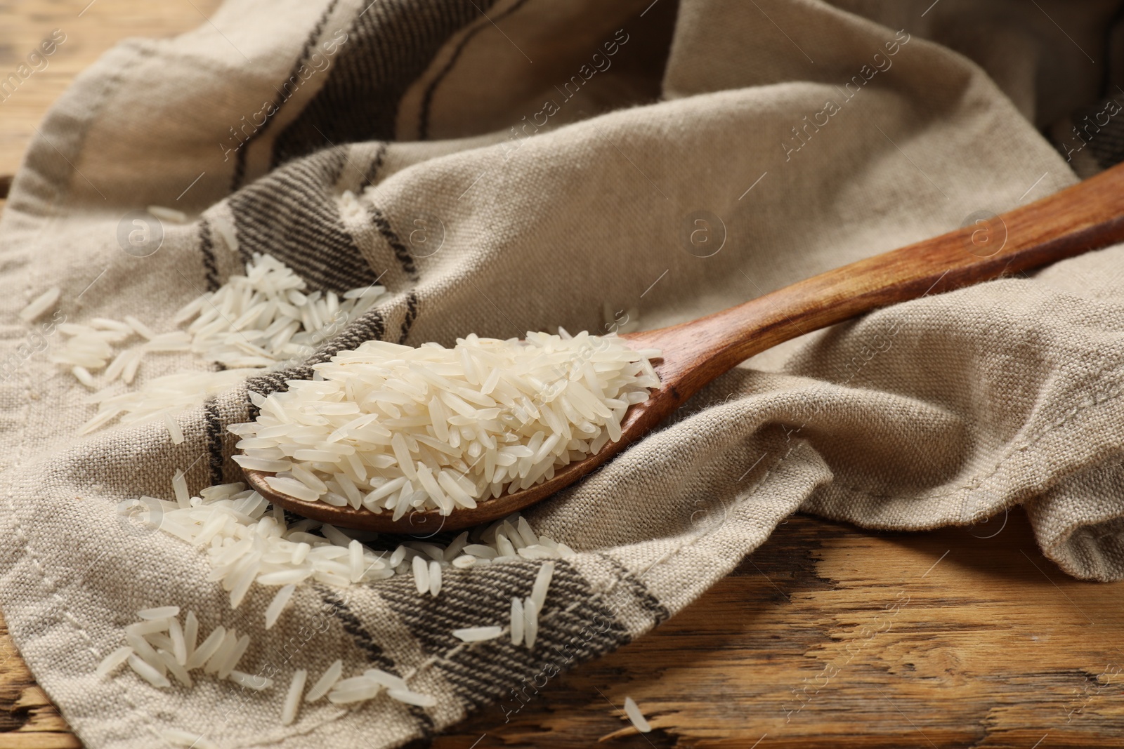 Photo of Raw basmati rice in spoon on wooden table, closeup