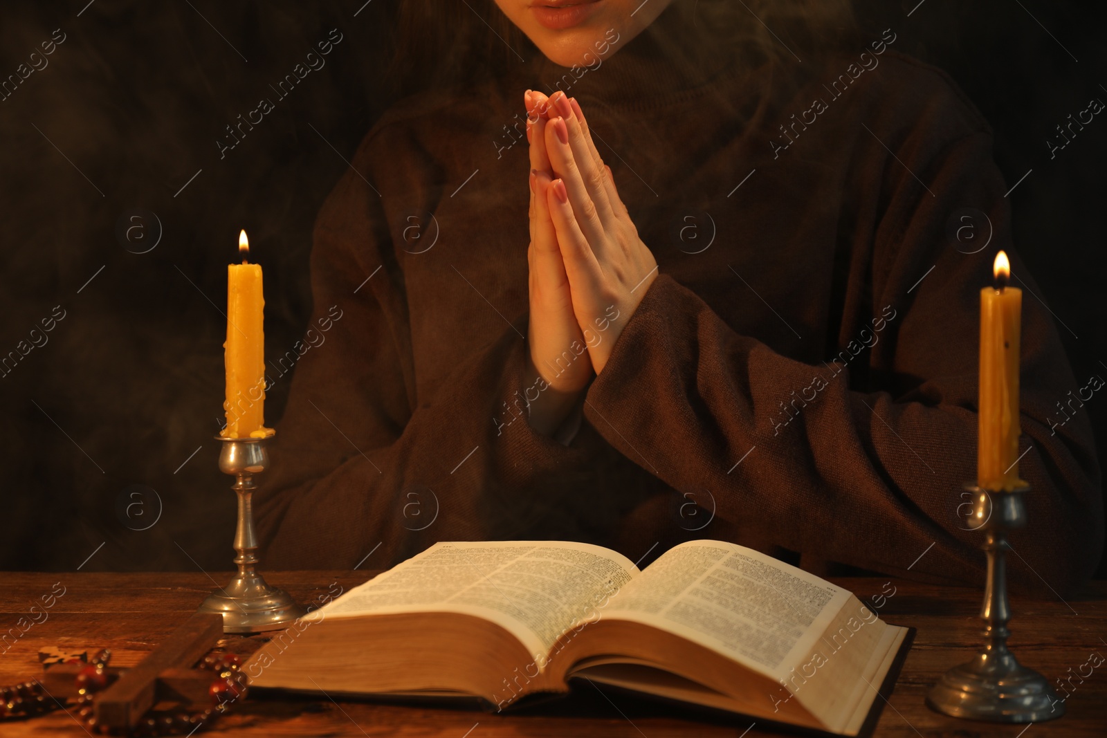 Photo of Woman praying at table with burning candles and Bible, closeup