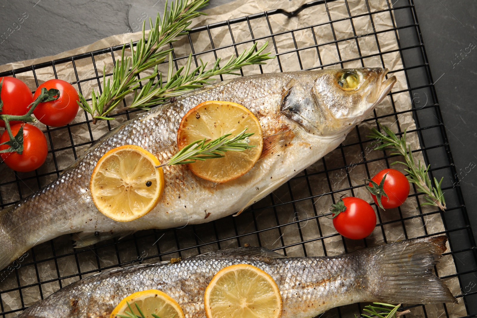 Photo of Baked fish with tomatoes, rosemary and lemon on black textured table, top view