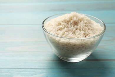 Photo of Raw basmati rice in bowl on light blue wooden table, space for text