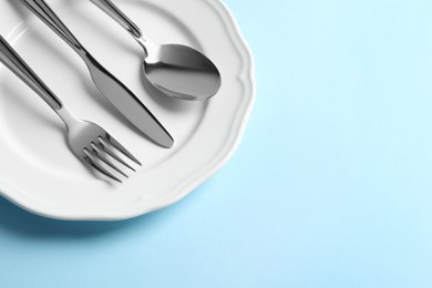 Stylish silver cutlery and plate on light blue background, above view. Space for text