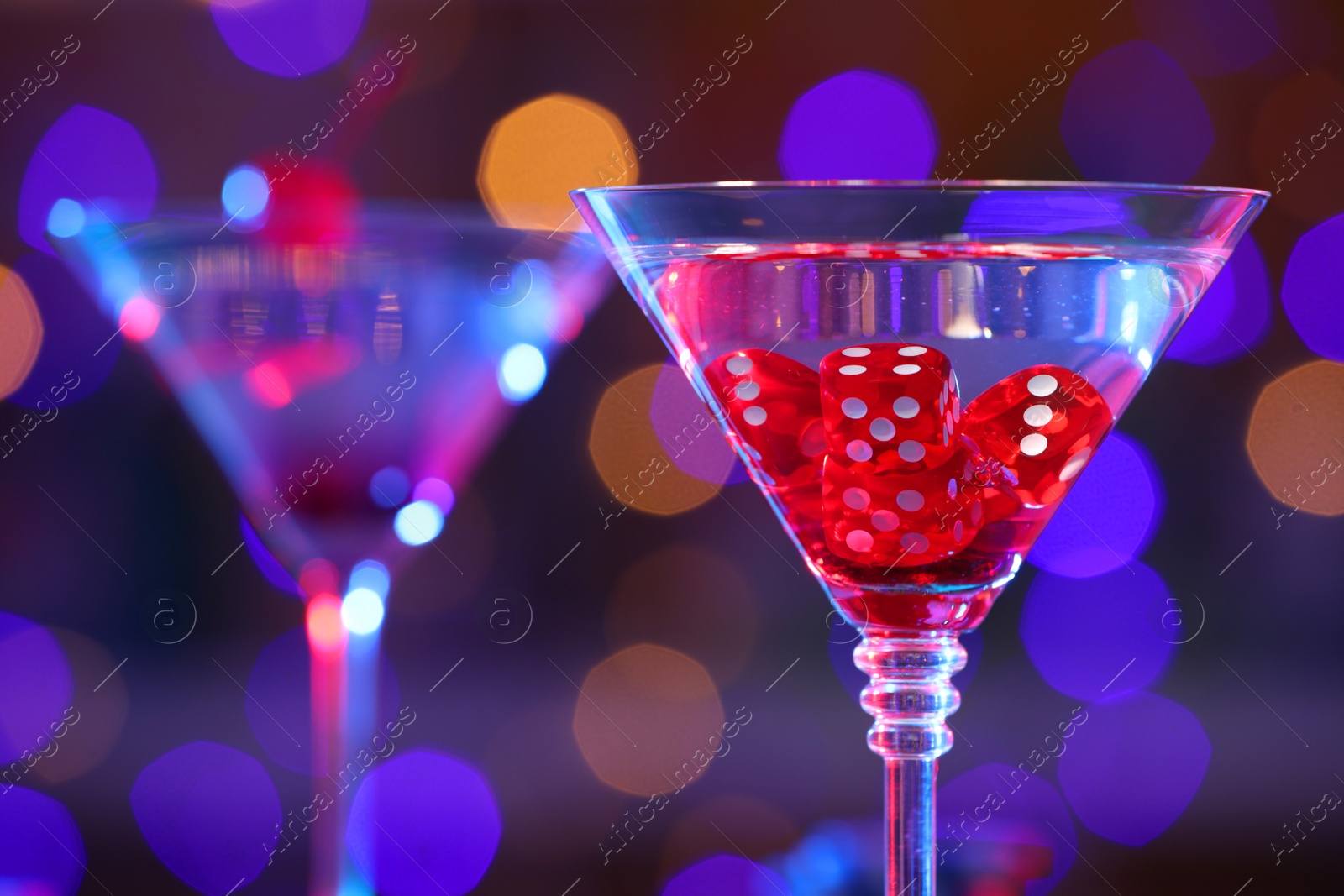 Photo of Cocktail with casino dice in glass against blurred lights, closeup. Space for text