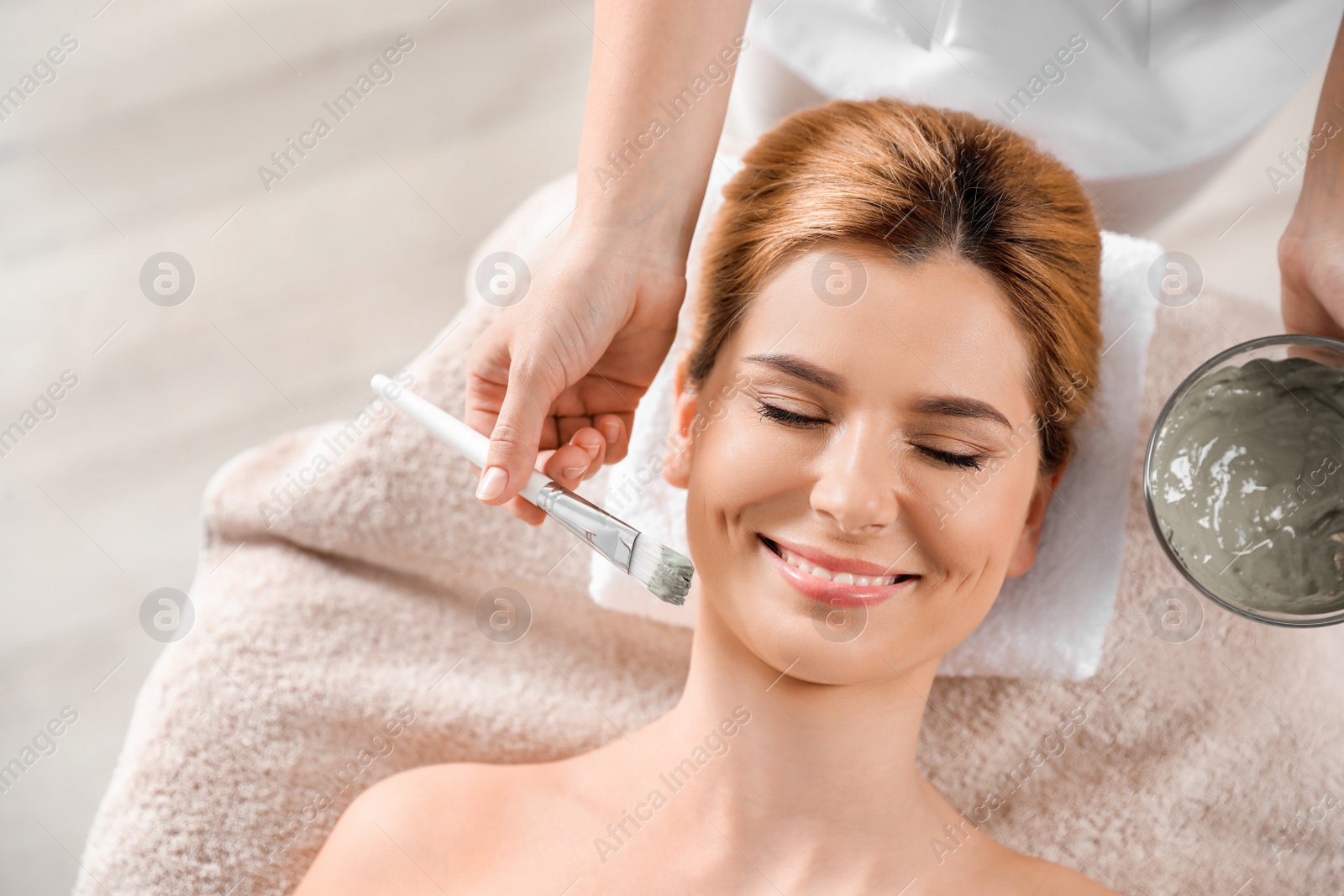 Photo of Cosmetologist applying mask onto woman's face in spa salon, top view