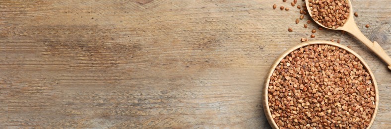 Image of Bowl and spoon of uncooked buckwheat on wooden table, top view with space for text. Banner design