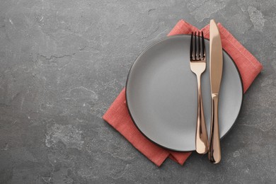 Photo of Clean plate, cutlery and napkin on grey textured table, top view. Space for text