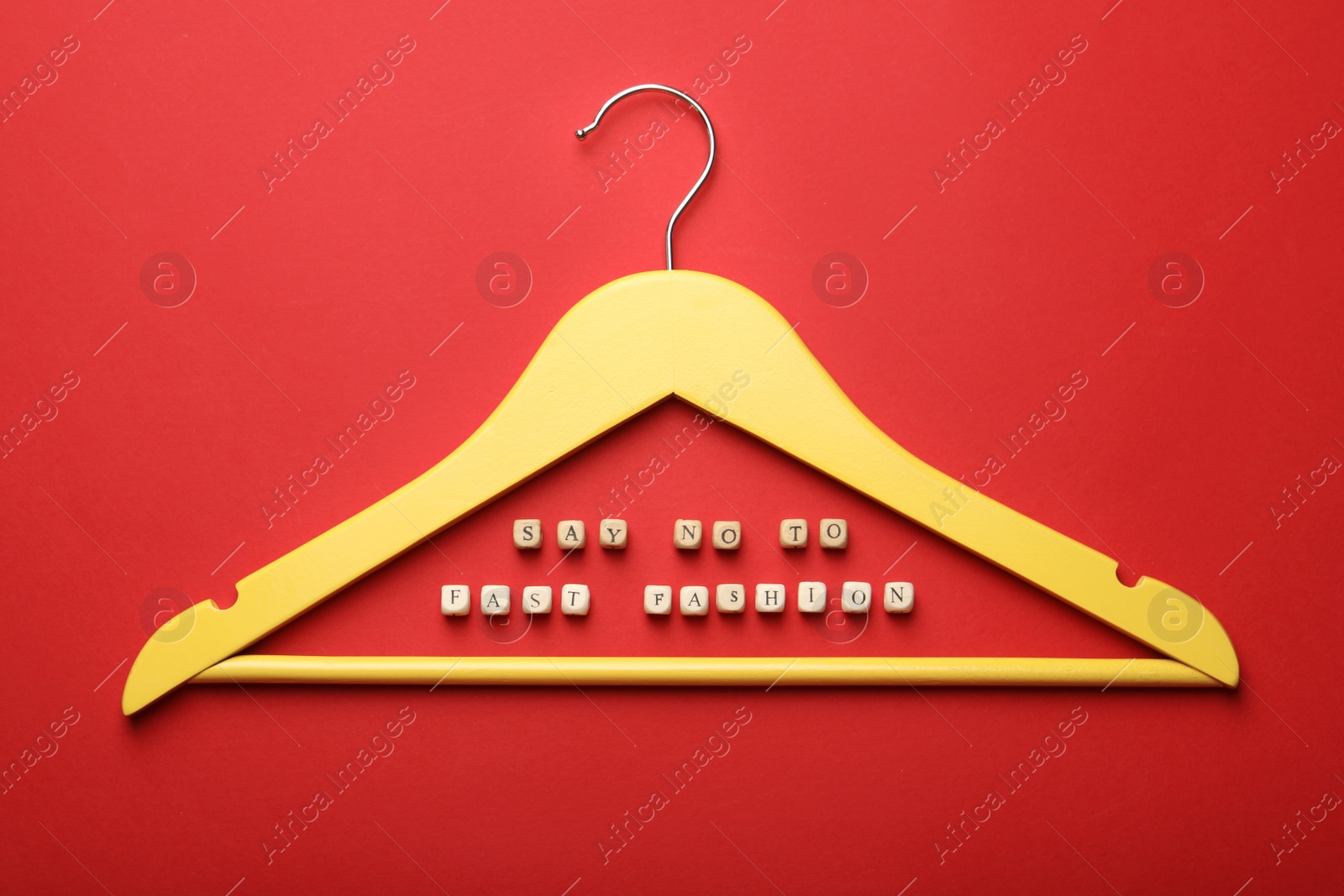 Photo of Wooden cubes with phrase Fast Fashion and yellow hanger on red background, top view