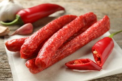 Photo of Thin dry smoked sausages and chili pepper on old wooden table, closeup