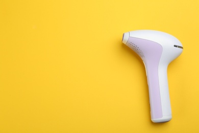 Modern photoepilator on yellow background, top view. Space for text