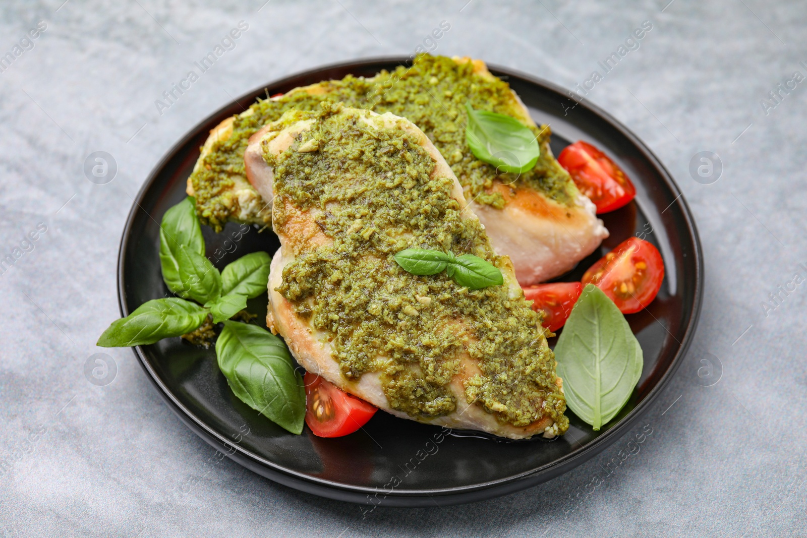 Photo of Delicious chicken breasts with pesto sauce, tomatoes and basil on light gray table, closeup