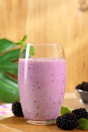 Photo of Delicious blackberry smoothie in glass and berries on wooden board, closeup
