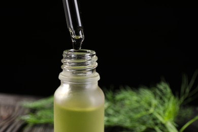 Photo of Dripping dill essential oil from pipette into bottle against black background, closeup. Space for text