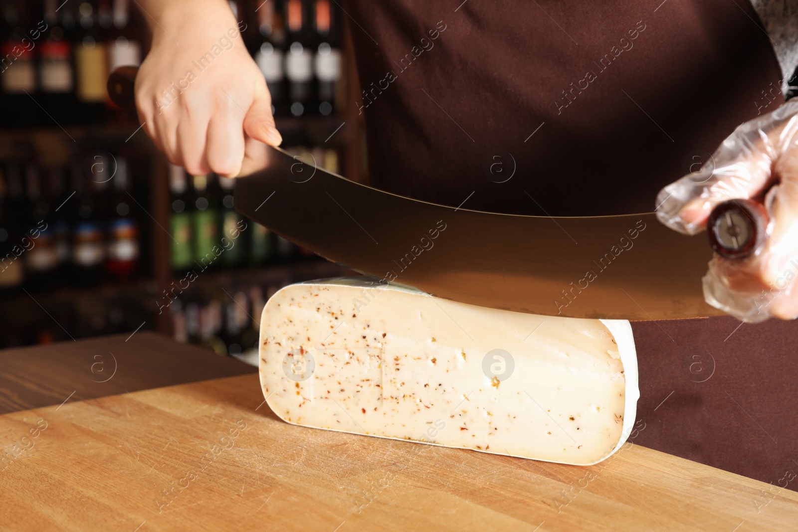 Photo of Seller cutting delicious cheese on table in store