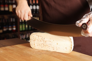 Photo of Seller cutting delicious cheese on table in store