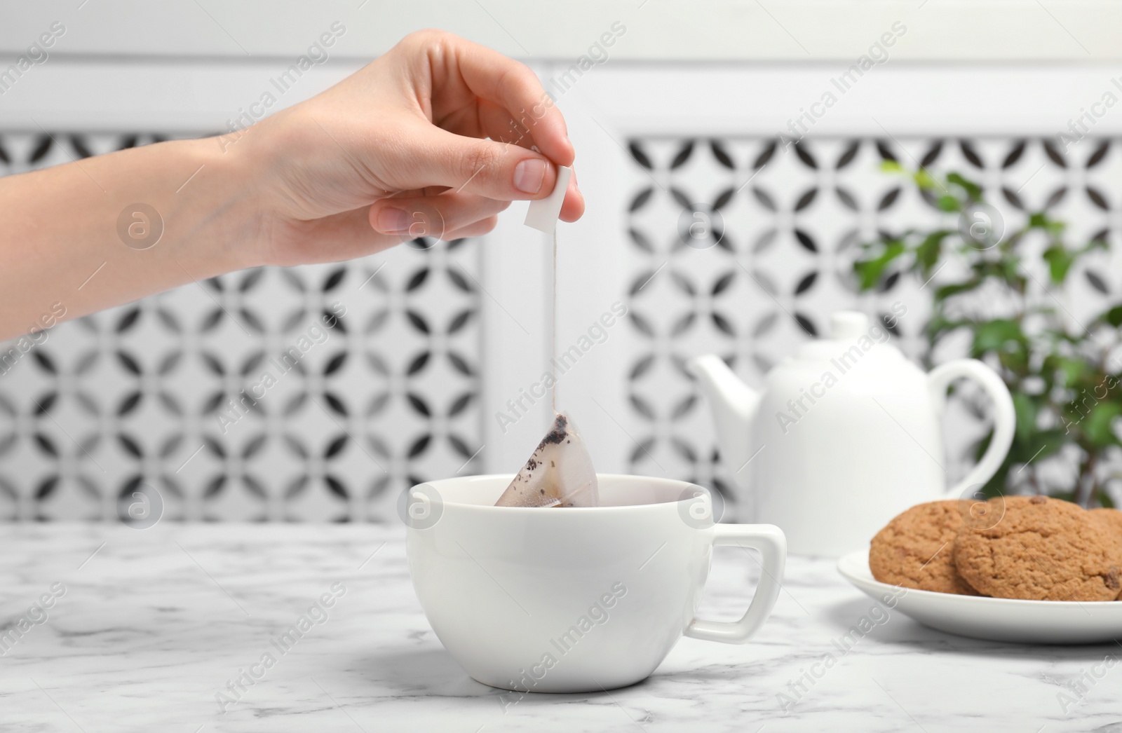 Photo of Woman brewing tea with bag in cup on table, closeup