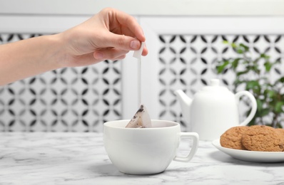 Photo of Woman brewing tea with bag in cup on table, closeup