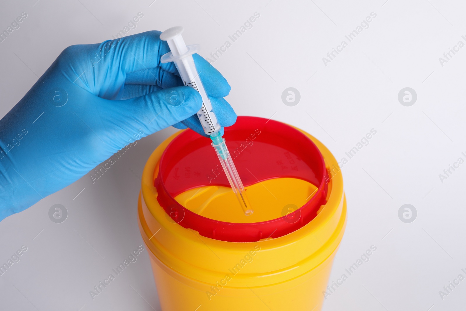 Photo of Doctor throwing used syringe into sharps container on white background, closeup