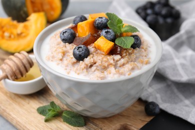 Photo of Tasty wheat porridge with pumpkin, dates and blueberries in bowl on table, closeup