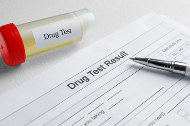 Photo of Drug test result form, container with urine sample and pen on light table, closeup