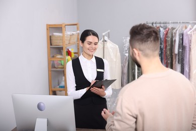 Photo of Dry-cleaning service. Happy woman working with client indoors