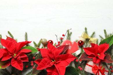 Flat lay composition with poinsettias (traditional Christmas flowers) and holiday decor on white wooden table. Space for text