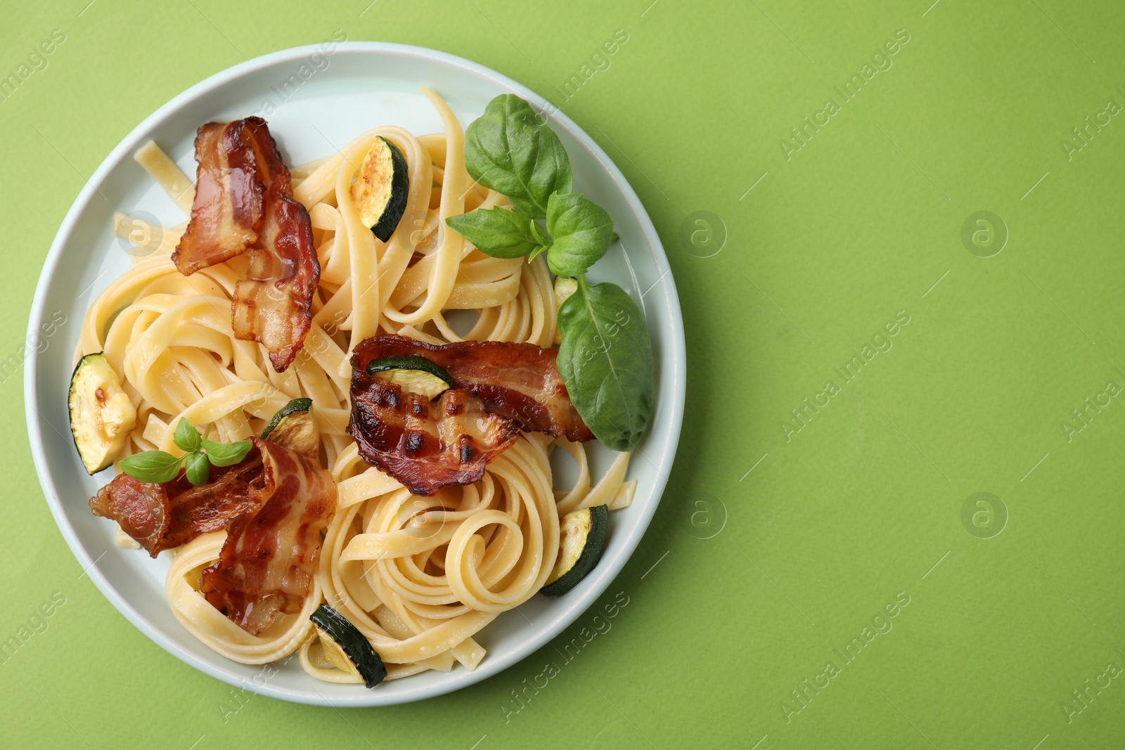 Photo of Tasty pasta with bacon and basil on light green table, top view. Space for text