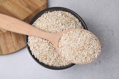 Dry barley groats in bowl and spoon on light grey table, top view