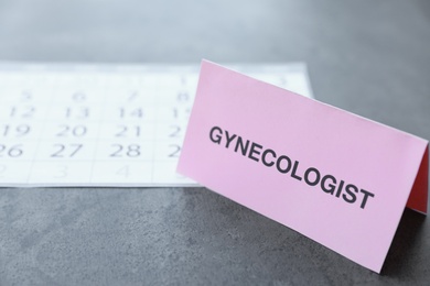 Card with word GYNECOLOGIST near calendar on table