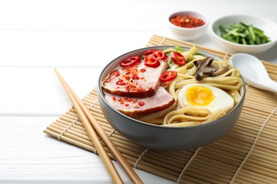 Photo of Delicious ramen in bowl and chopsticks on white wooden table, space for text. Noodle soup