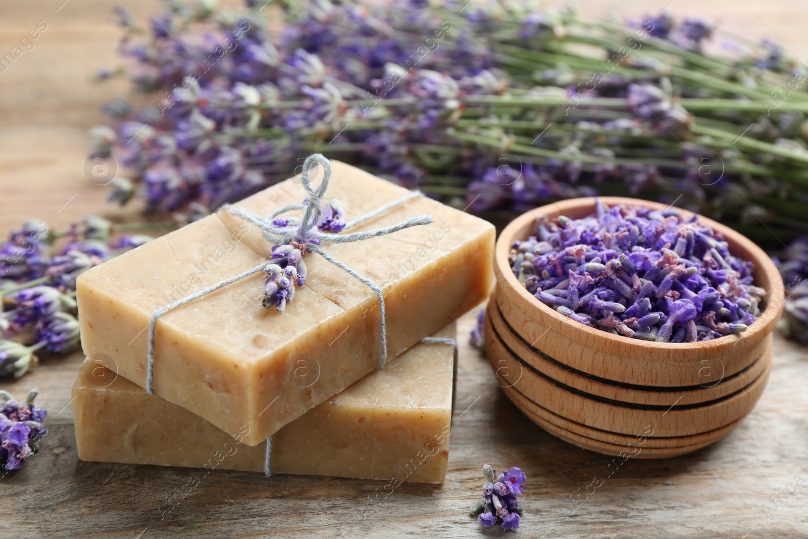 Photo of Handmade soap bars with lavender flowers on brown wooden table, closeup