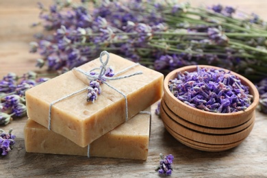 Handmade soap bars with lavender flowers on brown wooden table, closeup
