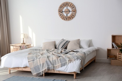 Bed with pillows and plaid in modern room interior