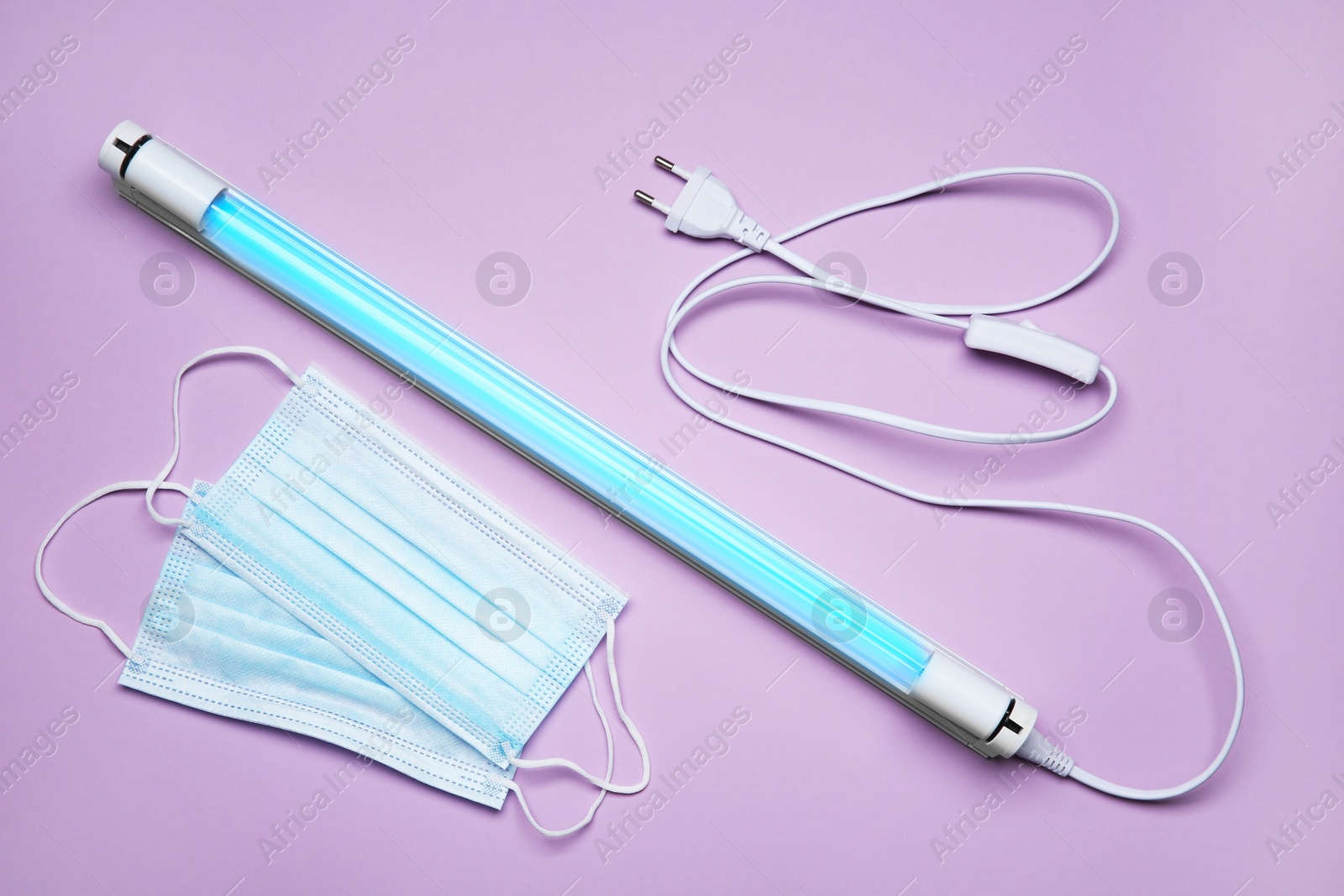 Photo of Ultraviolet lamp and medical masks on violet background, flat lay