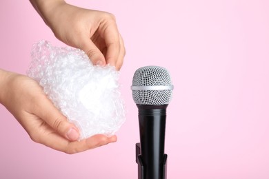 Woman making ASMR sounds with microphone and bubble wrap on pink background, closeup