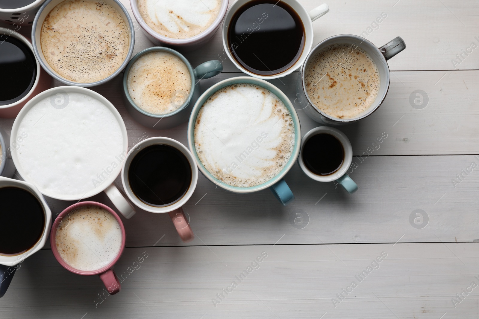 Photo of Many different cups with aromatic hot coffee on white wooden table, flat lay