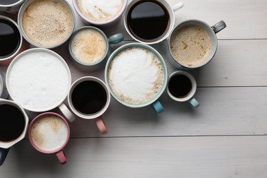 Many different cups with aromatic hot coffee on white wooden table, flat lay