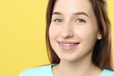 Portrait of smiling woman with dental braces on yellow background, closeup. Space for text