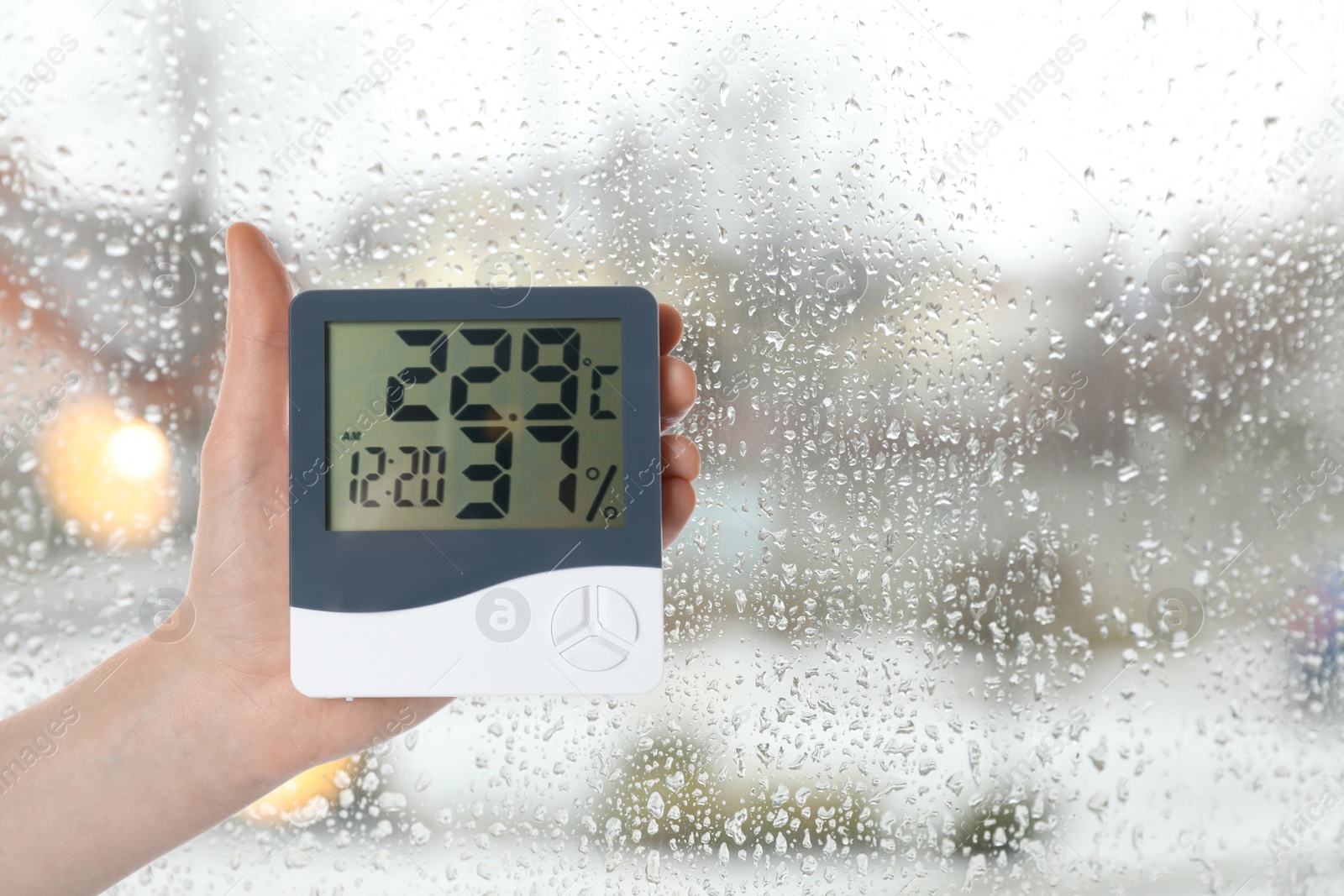 Image of Woman holding digital hygrometer with thermometer near window on rainy day, closeup. Space for text